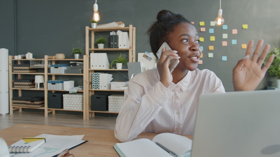 Young woman talking on phone at desk with laptop.