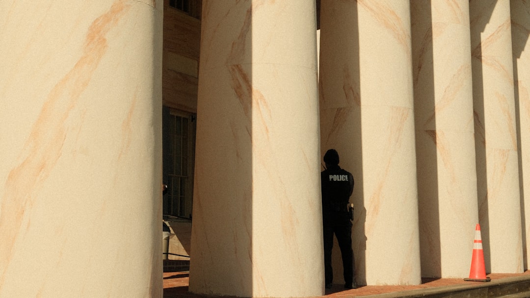 A person in uniform stands between large stone columns.