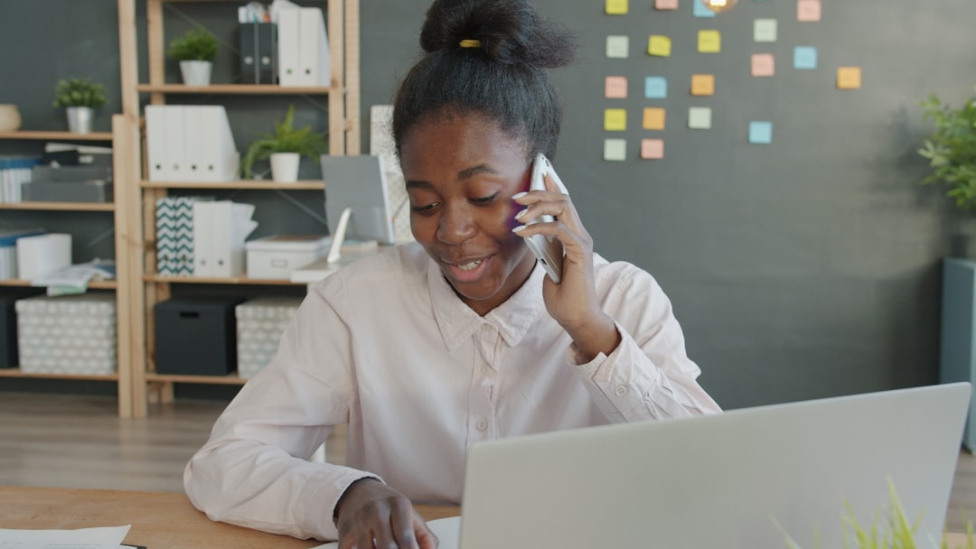 Young woman talking on phone at office desk with laptop.