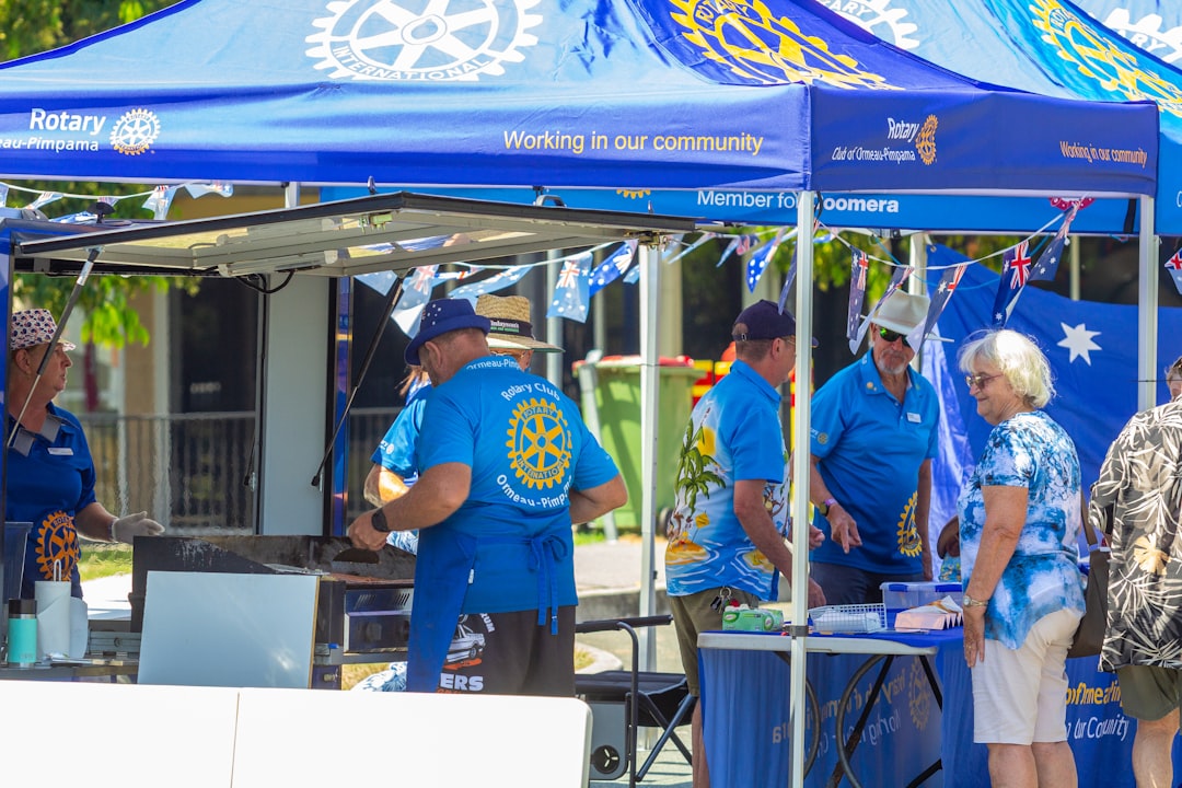 People gathered under blue rotary tents at an outdoor event.